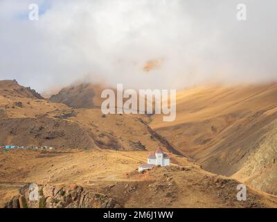 Une vue sur la maison blanche avec ses petites fenêtres et son toit rouge se dresse en hauteur dans les montagnes où les nuages descendent sur la montagne Banque D'Images