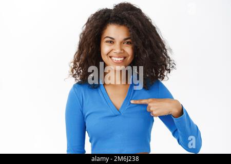 Souriante Femme noire se pointant vers elle avec confiance, présentez-la, debout sur fond blanc Banque D'Images