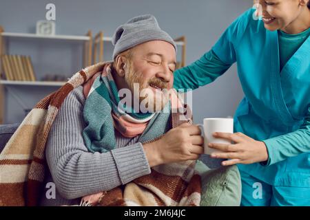 Infirmière prenant soin d'un homme âgé retraité malade, l'aidant et lui faisant du thé chaud Banque D'Images