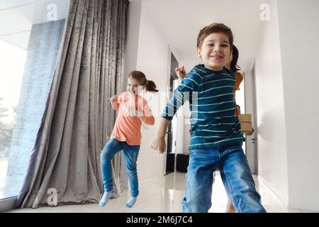 Bonne famille dans le hall. Drôle d'enfants sautant avec boîte en carton, les parents riant, Banque D'Images