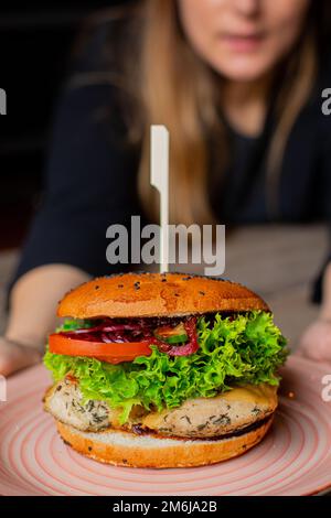 Plaque de gros plan avec hamburger de poulet appétissant juteux isolé sur fond de serveur, mise au point sélective. Servir un gros sandwich calorique sur une brochette. Comme Banque D'Images