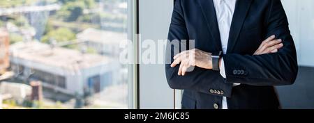 Homme d'affaires mature et confiant, méconnaissable, avec bras pliés au bureau près de la fenêtre, du panorama, de l'espace de copie Banque D'Images