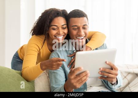 Joyeuse femme afro-américaine du millénaire, regardant la tablette, passer des appels vidéo, utiliser l'application Banque D'Images