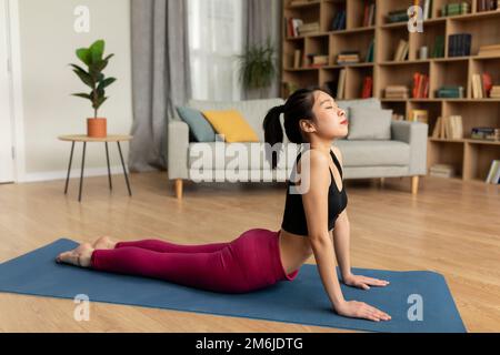 FIT femme coréenne faisant le yoga cobra pose ou pilates, s'entraîner sur le tapis dans le salon intérieur, espace de copie Banque D'Images