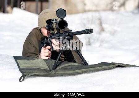 Un fusil de sniper avec une vue optique dans les mains de l'homme visant à poser la vue de face d'hiver Banque D'Images