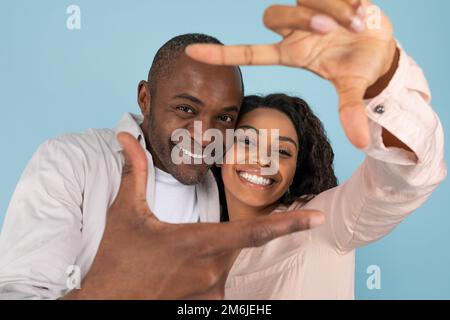 Capturer des moments. Gros plan portrait d'un couple noir en faisant un cadre photo avec les doigts, en regardant l'appareil photo et en souriant Banque D'Images