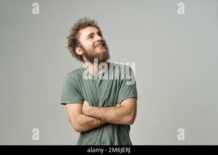 Jeune homme souriant et beau avec des cheveux barbes et sauvages bouclés, des yeux bleu vif regardant avec les mains repliées isolés sur le bac blanc Banque D'Images