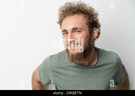 Beau sourire jeune beau barbu sauvage bouclés cheveux homme avec des yeux bleu vif isolé sur fond blanc. Jeune pensée m Banque D'Images