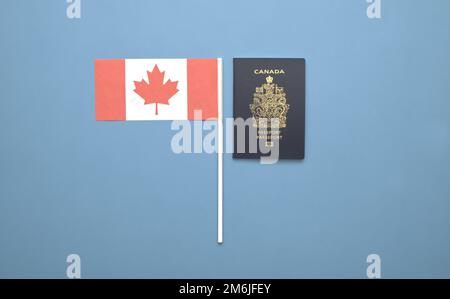 Un passeport canadien à côté d'un drapeau canadien sur fond bleu clair et solide Banque D'Images