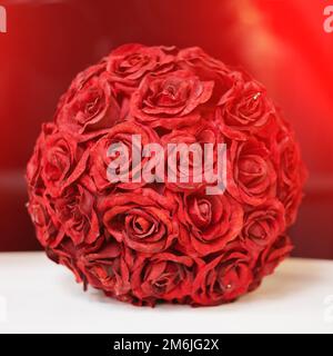 Une boule décorative de boutons roses rouges se dresse sur une surface blanche sur un fond rouge Banque D'Images