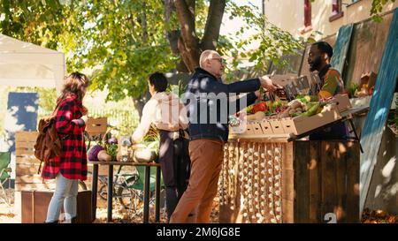 Personne âgée cherchant à acheter des produits naturels d'un fournisseur afro-américain, parlant de nutrition saine et de produits locaux. Homme senior achetant des fruits et des légumes au stand du marché. Banque D'Images