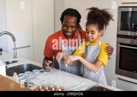 Papa noir affectueux et fille préparer de la pâte pour des muffins dans la cuisine Banque D'Images