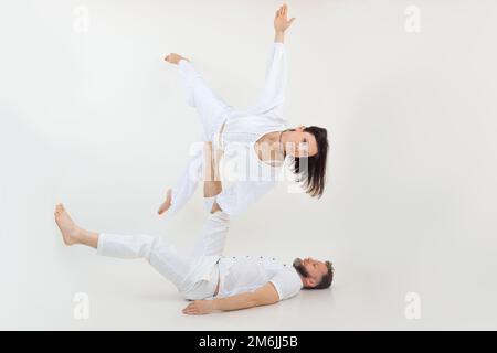 Couple sportif sur fond blanc. Homme d'âge moyen couché tenant une jeune femme qui s'étire la jambe, le bras, pratiquant acroyoga. Banque D'Images