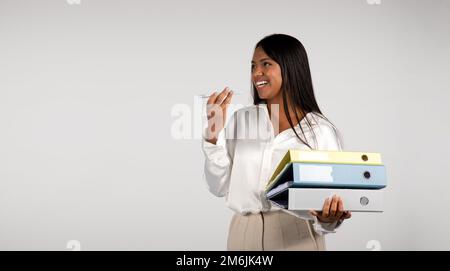 Bonne jeune femme d'affaires afro-américaine qui appelle par téléphone, parle, tient beaucoup de dossiers Banque D'Images