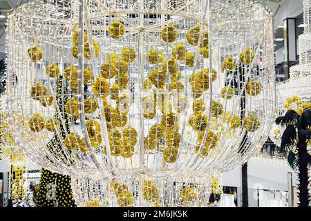 Un immense lustre décoré de boules de Noël dorées et d'une guirlande est suspendu dans un centre commercial festif Banque D'Images