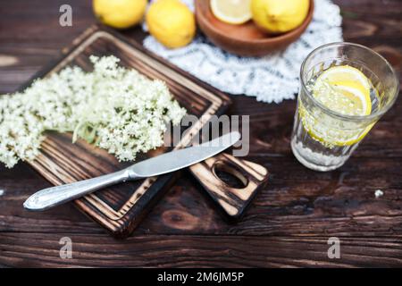 Broyage de citron et de sureau noir sur une planche à découper pour faire une boisson à base de plantes ou un médicament pour la guérison à la maison à partir de sirop de fleurs de sureau. Banque D'Images