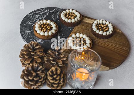 Vue de dessus de quatre tartes décorées de crème blanche et de perles dorées placées sur un tableau de deux couleurs. Quatre cônes flous et porte-bougie à l'avant. . Photo de haute qualité Banque D'Images