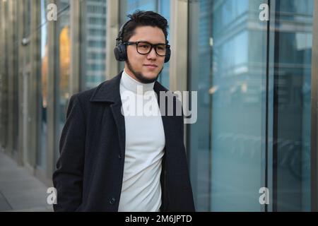 Un homme d'affaires asiatique dans un casque passe devant un immeuble de bureaux. Banque D'Images