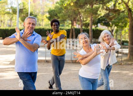Un entraîneur afro-américain positif aidant les personnes âgées à étirer leurs muscles avant de danser à l'extérieur dans le parc Banque D'Images