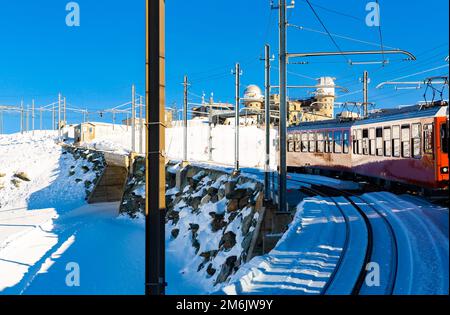 Train rouge à crémaillère approchant la gare dans les Alpes suisses le jour d'hiver Banque D'Images