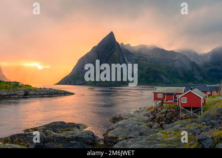 Coucher de soleil incroyable à travers la brume et le Mont Reinebringen sur les maisons rouges de Hamnoy, îles Lofoten, Norvège Banque D'Images