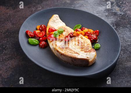 Steak d'espadon frit aux tomates et au paprika servi en gros plan sur une assiette design Banque D'Images