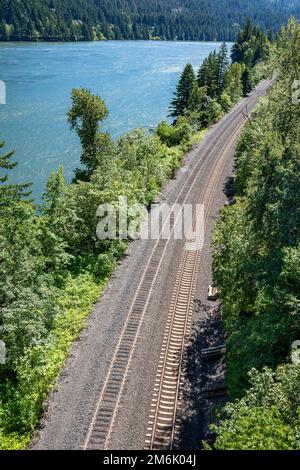 Paysage d'été pittoresque avec un sentier de chemin de fer de montagne sinueux qui longe la rive de la rivière Columbia dans la gorge de Columbia, permettant le transport de commer Banque D'Images