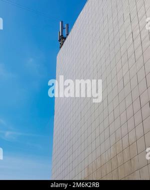 Le mur extérieur d'un bâtiment moderne de style commercial, lambrissé de tuiles, sur le toit des antennes modernes contre le ciel bleu Banque D'Images