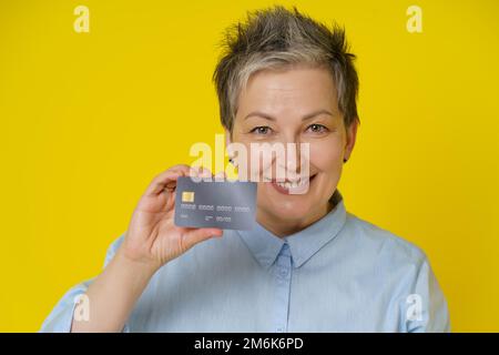 Portrait de la femme mûre grise avec crédit, carte de débit à la main faire le paiement en ligne ou le shopping en ligne, isolé sur yello Banque D'Images