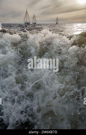 Éclaboussures d'eau de bateau à moteur en premier plan, yachts à voile au coucher du soleil en arrière-plan, régate de voile, grandes vagues Banque D'Images