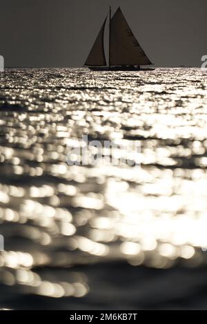 Yacht classique en mer au coucher du soleil, ciel clair, reflet du soleil sur l'eau Banque D'Images