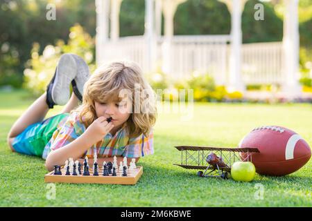 Jeux d'été et activités de plein air pour les enfants. Enfant garçon concentré développant une stratégie d'échecs, jouant au jeu de société dans l'arrière-cour, posant sur l'herbe. Banque D'Images