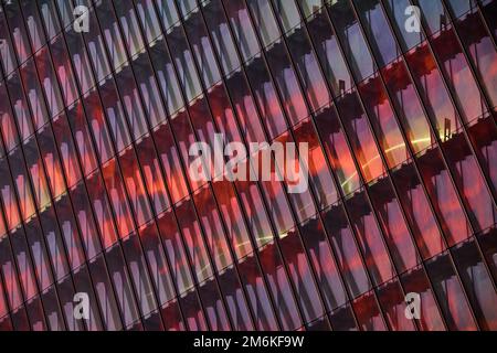 La façade en verre et en fer d'un énorme gratte-ciel au coucher du soleil, acier, couleur orange, reflet du soleil Banque D'Images