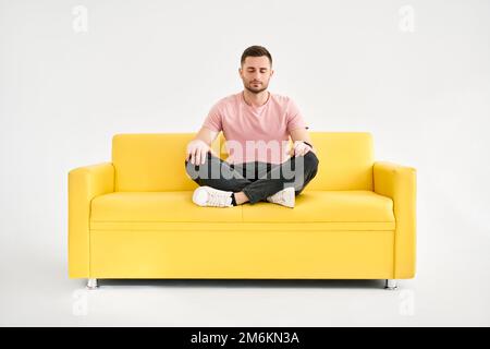 Beau jeune homme assis dans le yoga lotus poser et méditer sur le confortable canapé jaune Banque D'Images