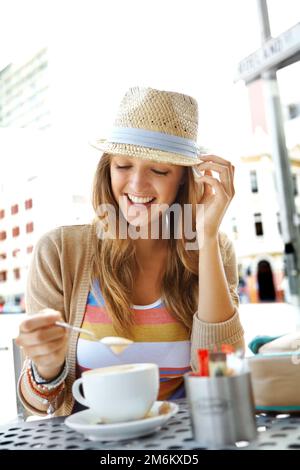 Des produits fraîchement préparés. Une jeune femme remuant son cappuccino tout en s'asseyant dans un café-terrasse de la ville. Banque D'Images