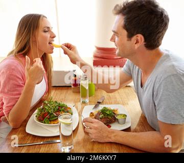 C'est mieux qu'une salade. Un beau jeune homme qui donne à sa petite amie un aperçu de sa nourriture pendant qu'ils déjeunent ensemble dans un restaurant. Banque D'Images