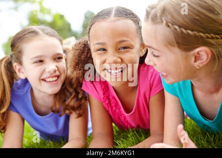 C'est un trio génial. Trois jeunes filles multi-ethniques allongé sur l'herbe dans un parc souriant à la caméra. Banque D'Images