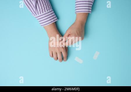 Pansement médical adhésif marron et main femelle pour le traitement des blessures et des coupures sur la peau, fond bleu Banque D'Images