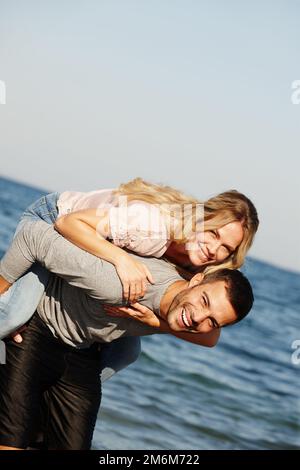 Nous nous amusons partout. Portrait d'un beau jeune homme donnant à sa petite amie un porcgyback à la plage. Banque D'Images