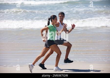 De bonnes choses viennent à ceux qui suent. un jeune couple jogging ensemble sur la plage. Banque D'Images