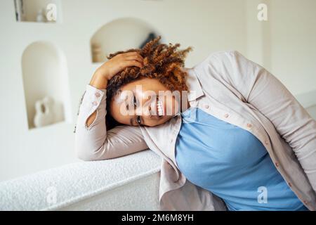 Jeune fille millénaire afro-américaine, heureuse et heureuse, asseyez-vous sur un canapé confortable dans un salon moderne et confortable Banque D'Images