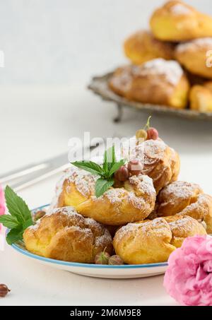 Eclairs cuits à la crème anglaise sur une plaque ronde en métal parsemée de sucre en poudre Banque D'Images