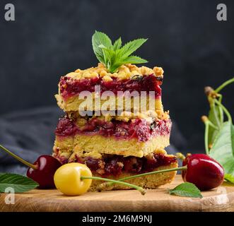 Des tranches carrées de crumble de cerise se trouvent dans une pile sur un fond noir Banque D'Images