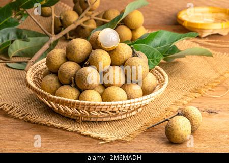 Pile de langan frais dans un panier en bambou avec bouquet de feuilles de longan et vertes. Banque D'Images