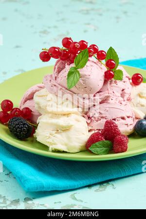 La glace à la vanille et à la framboise se ramasse sur une assiette ronde verte Banque D'Images