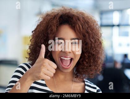 Vous allez très bien. Jeune femme donnant un signe de pouce vers le haut avec un grand sourire dans un bureau. Banque D'Images