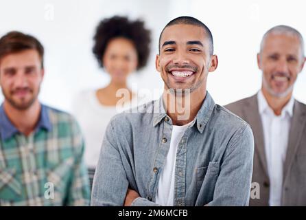 Les travaux les plus difficiles ont été payés avec le bon travail. Portrait d'un jeune homme souriant avec des collègues en arrière-plan. Banque D'Images