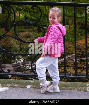 Portrait jolie belle petite fille en veste rose posant parc ville automne Banque D'Images