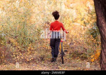 Activité le week-end en automne. Jeune heureuse femme souriante de course mixte avec vélo dans la forêt d'automne. Vue arrière de positif actif Banque D'Images
