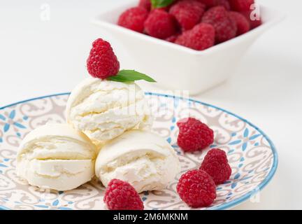 Boules de glace à la vanille aux framboises rouges dans une assiette ronde Banque D'Images